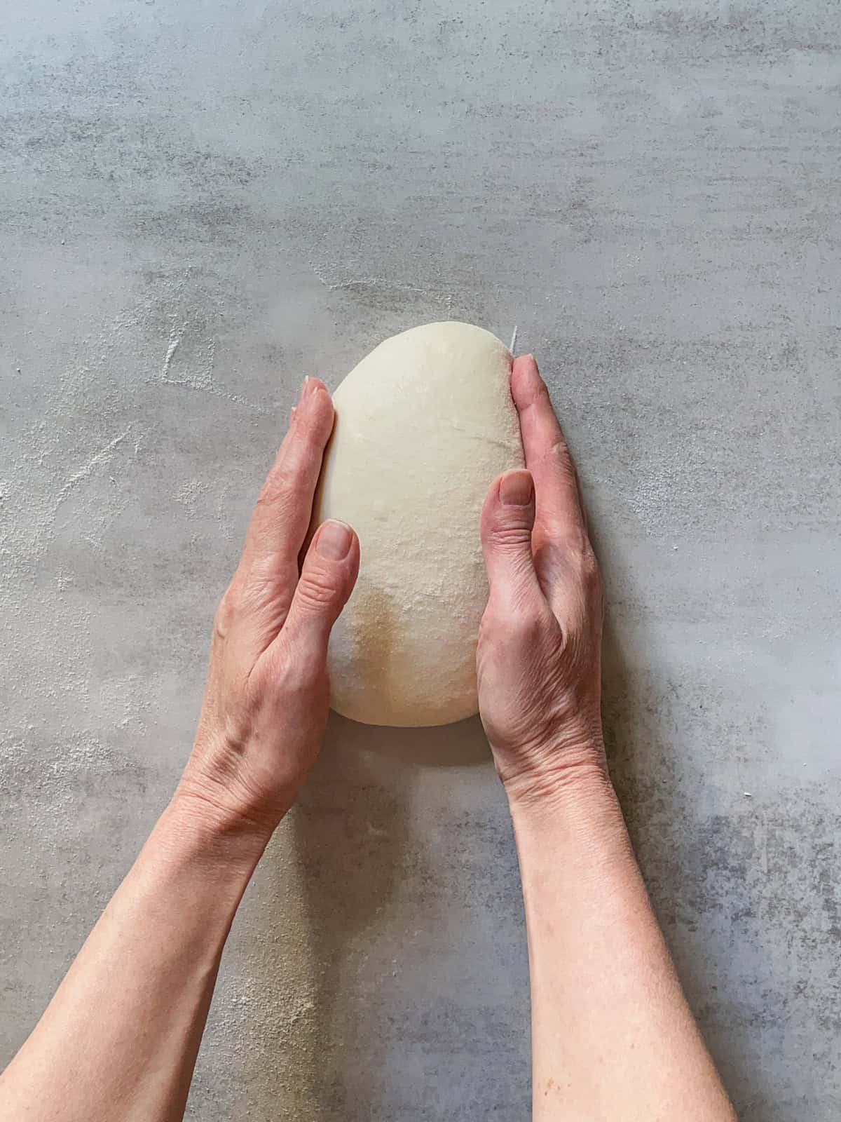 Hands turning a ball of bread dough.