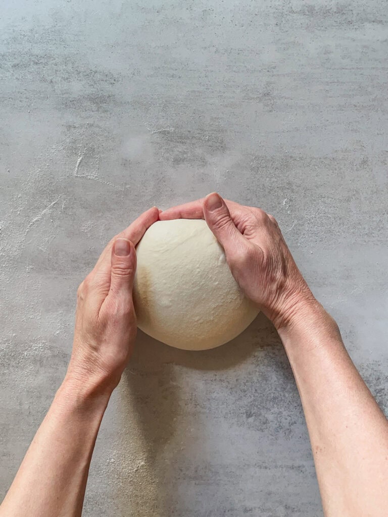 Hands pushing a ball of bread dough.