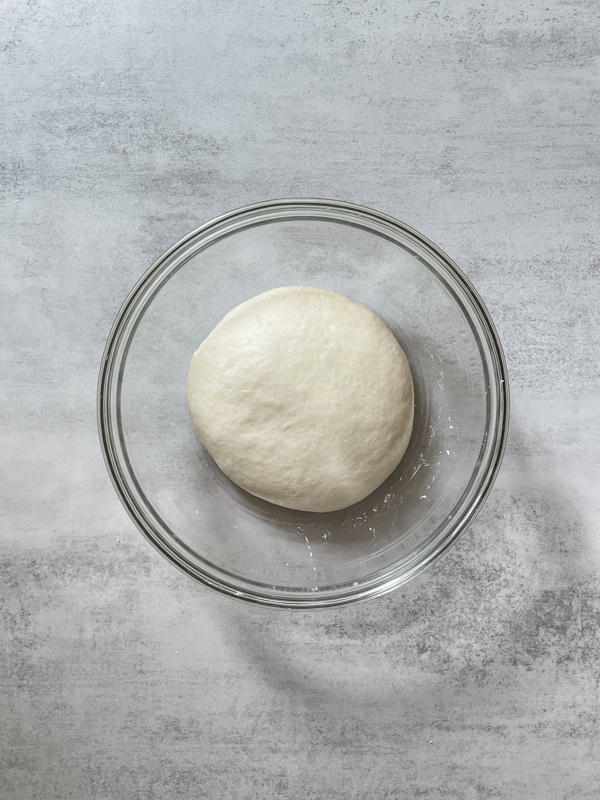 Mixed dough shaped into a ball in a glass bowl.