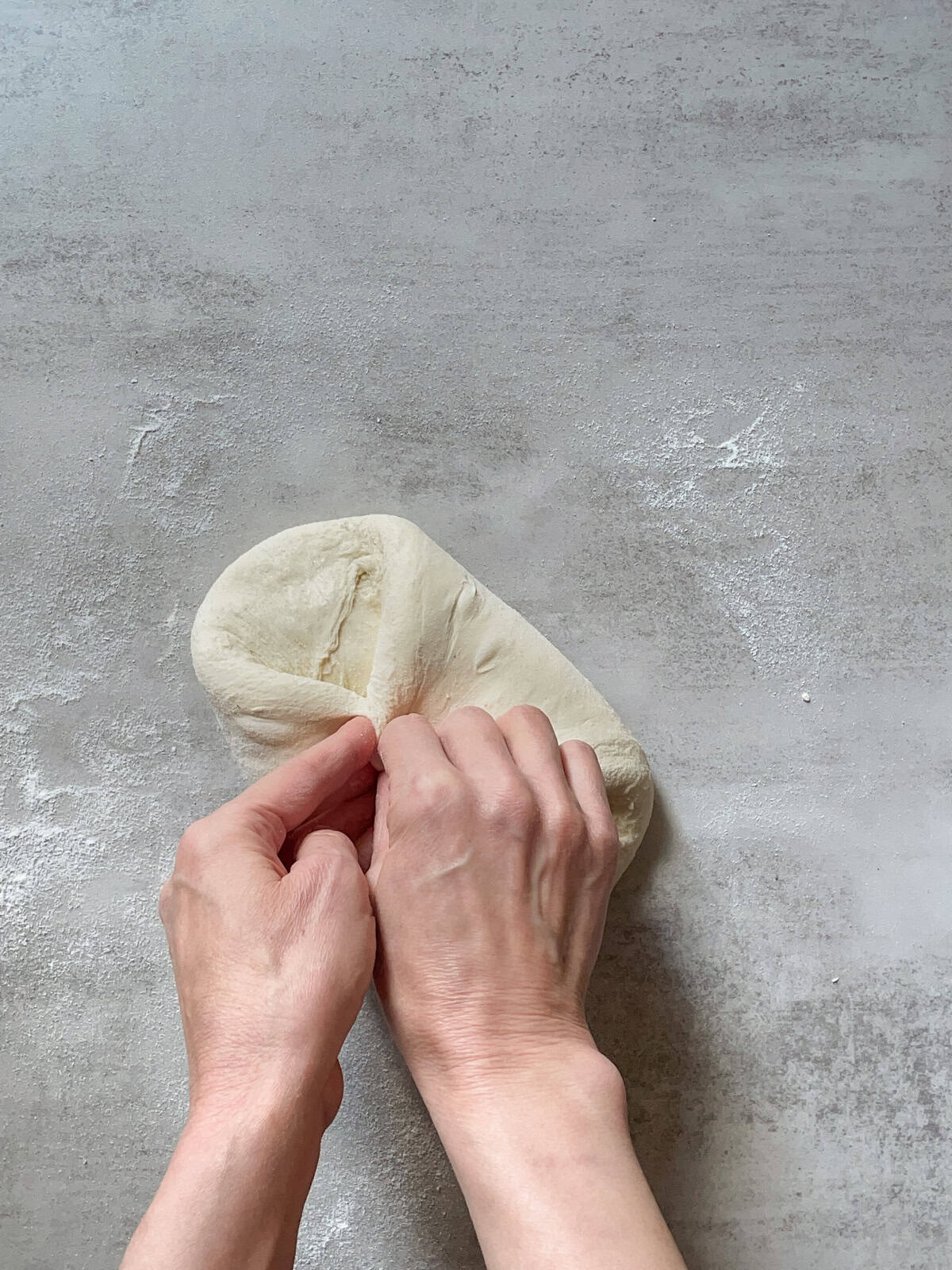 Hands folding the right and left sides of the dough toward the center.