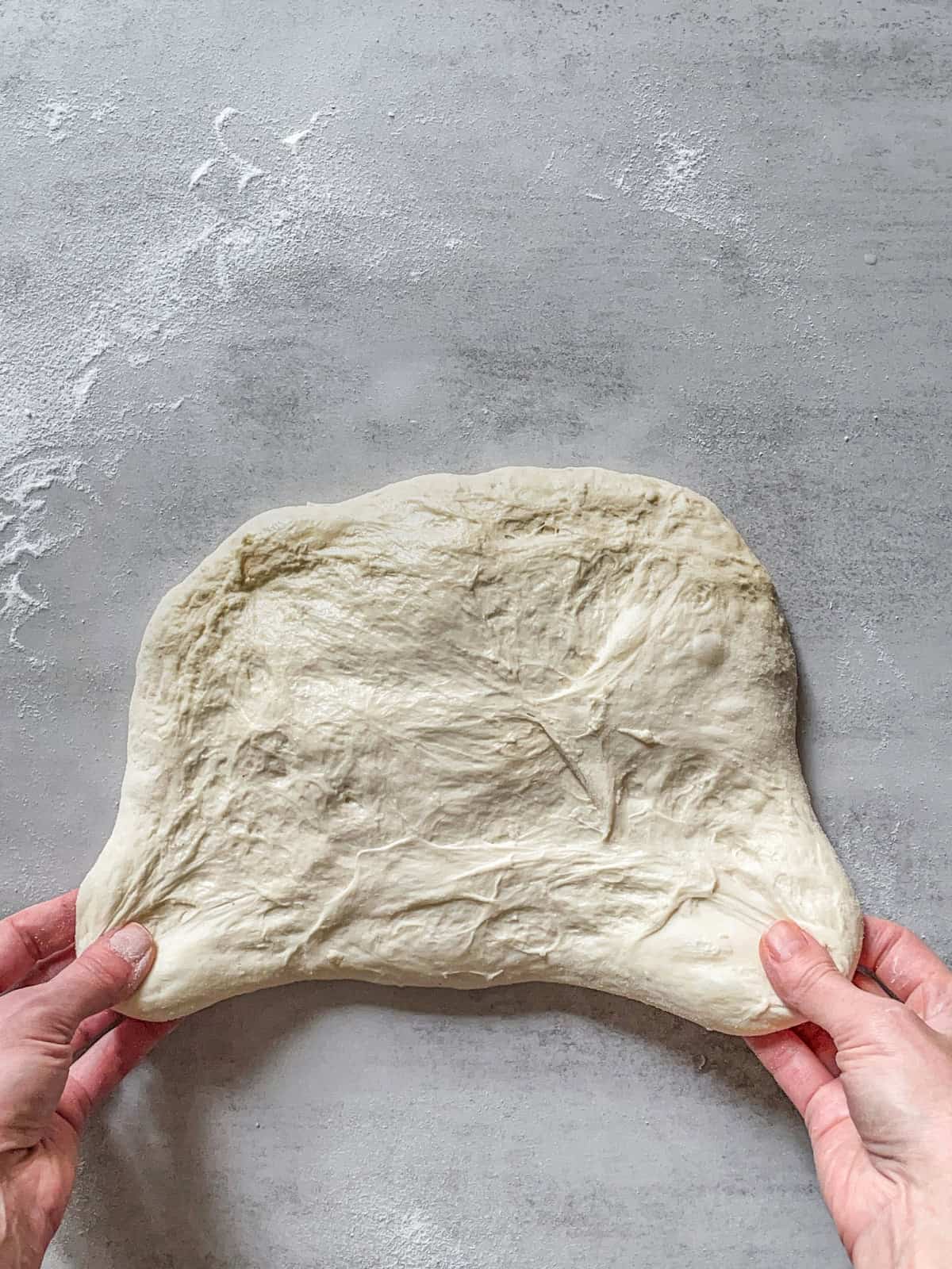 Hands stretching the sides of the bread dough.