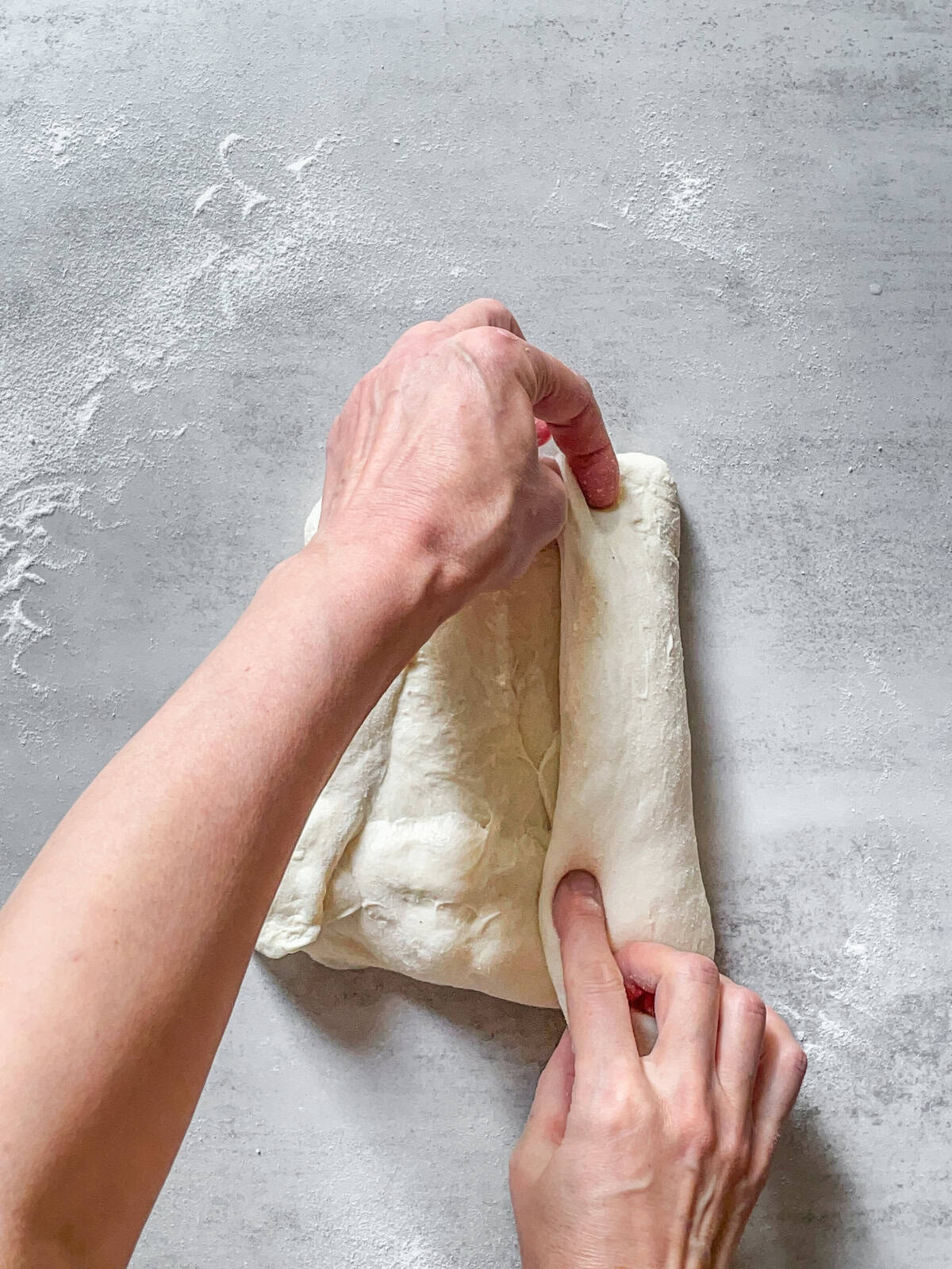 Hands folding the right side of the dough toward the middle.