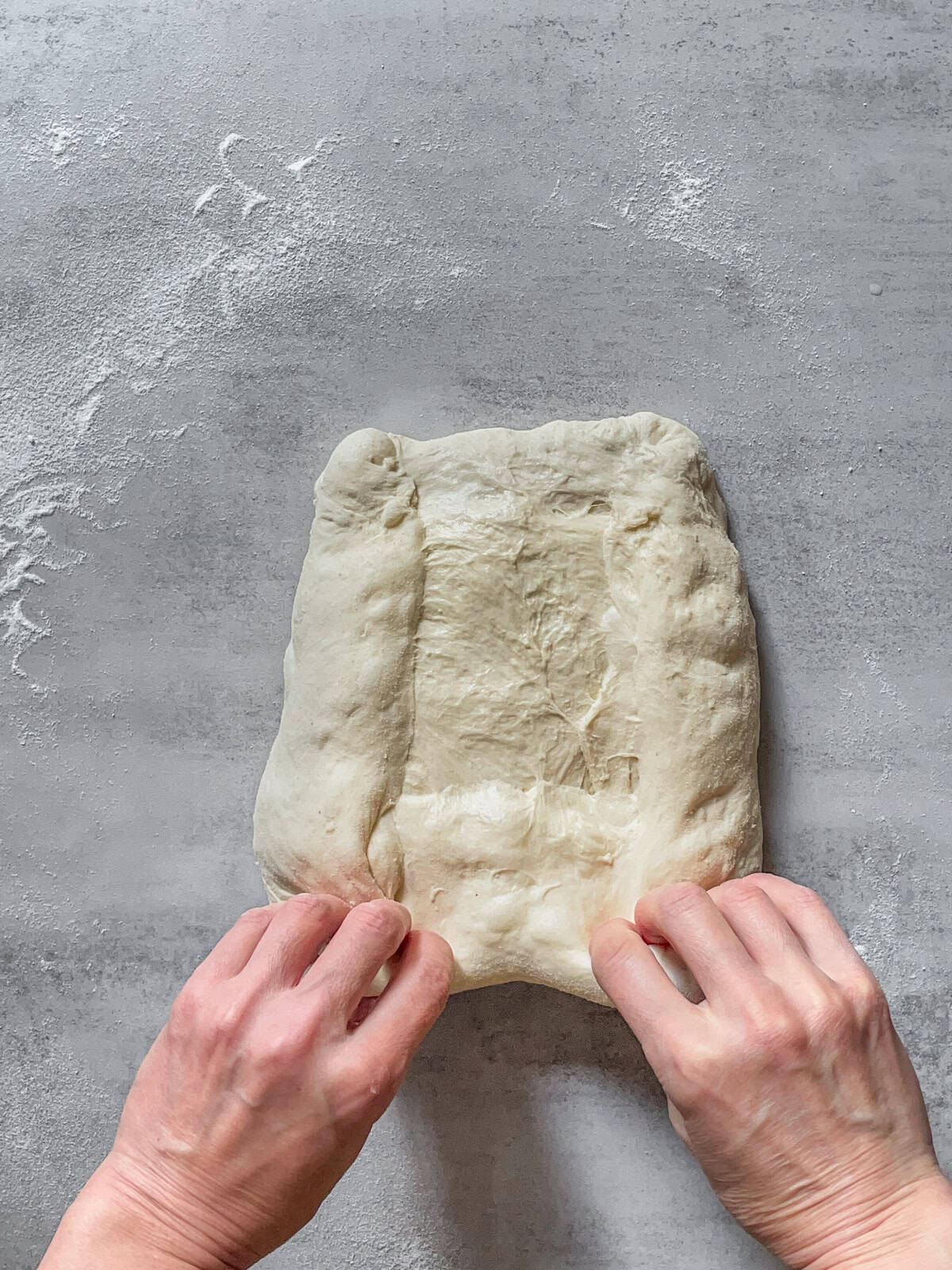 Hands beginning to pull the bottom of the dough upward.