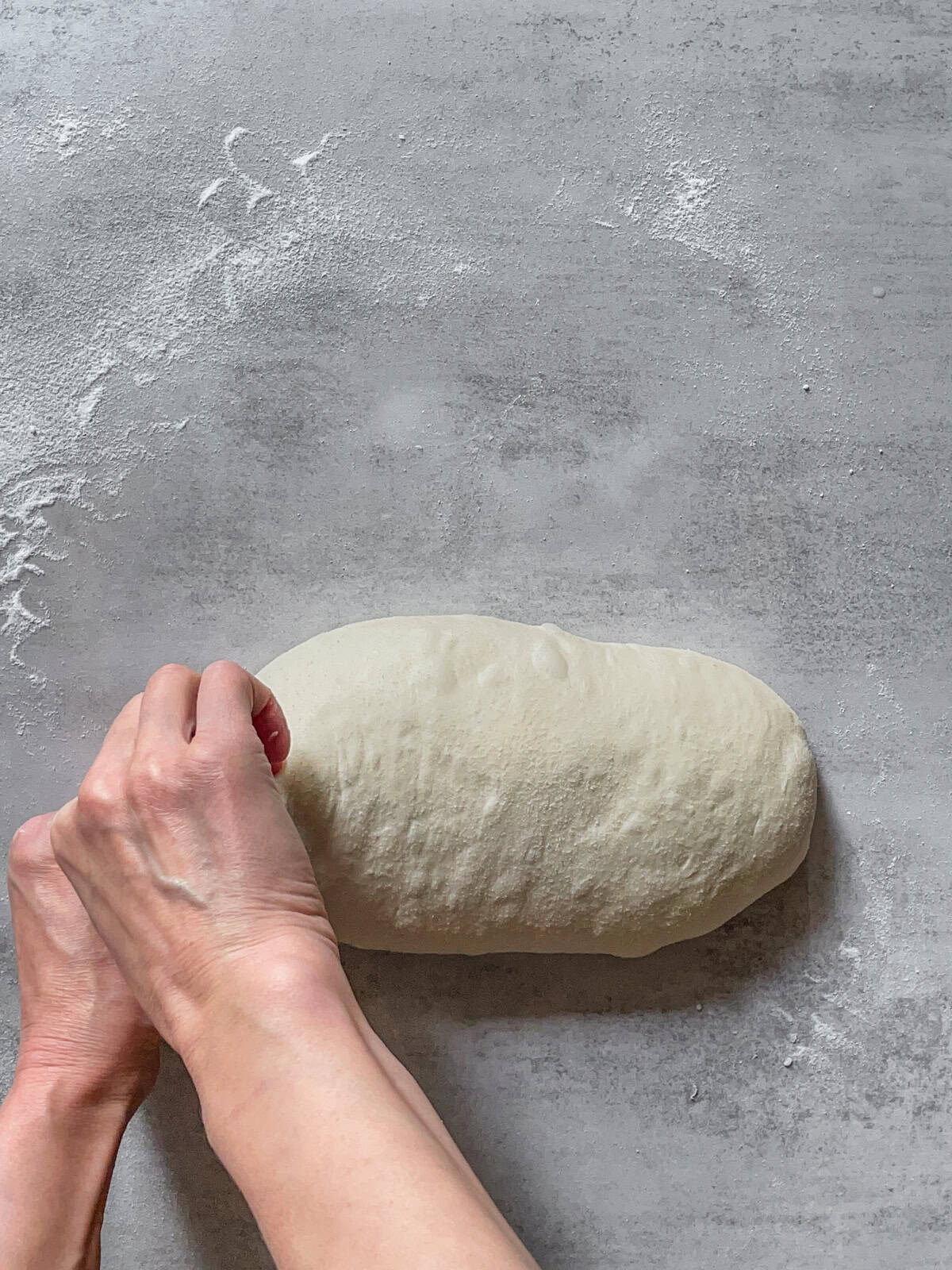 Hands stitching the ends of the dough to close them.
