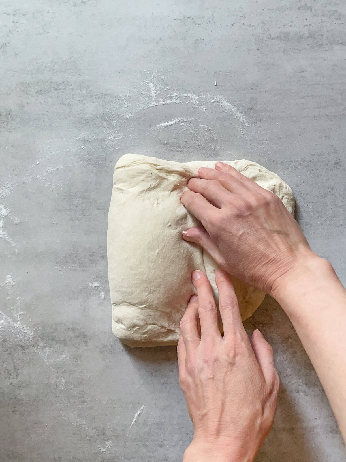 Hands folding the left side of the dough to the center.