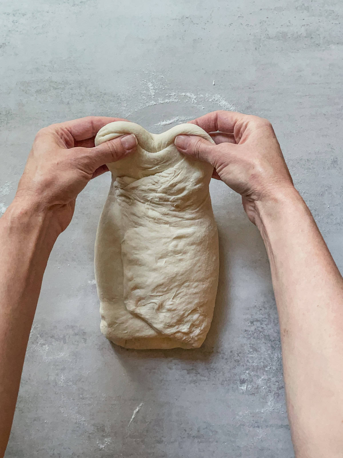 Hands pulling the top of the dough.