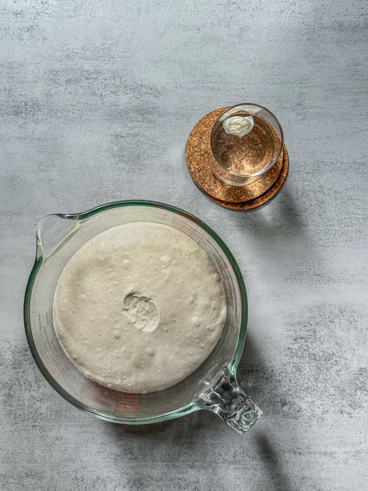 Dough floating in a glass, next to a larger cup of dough.
