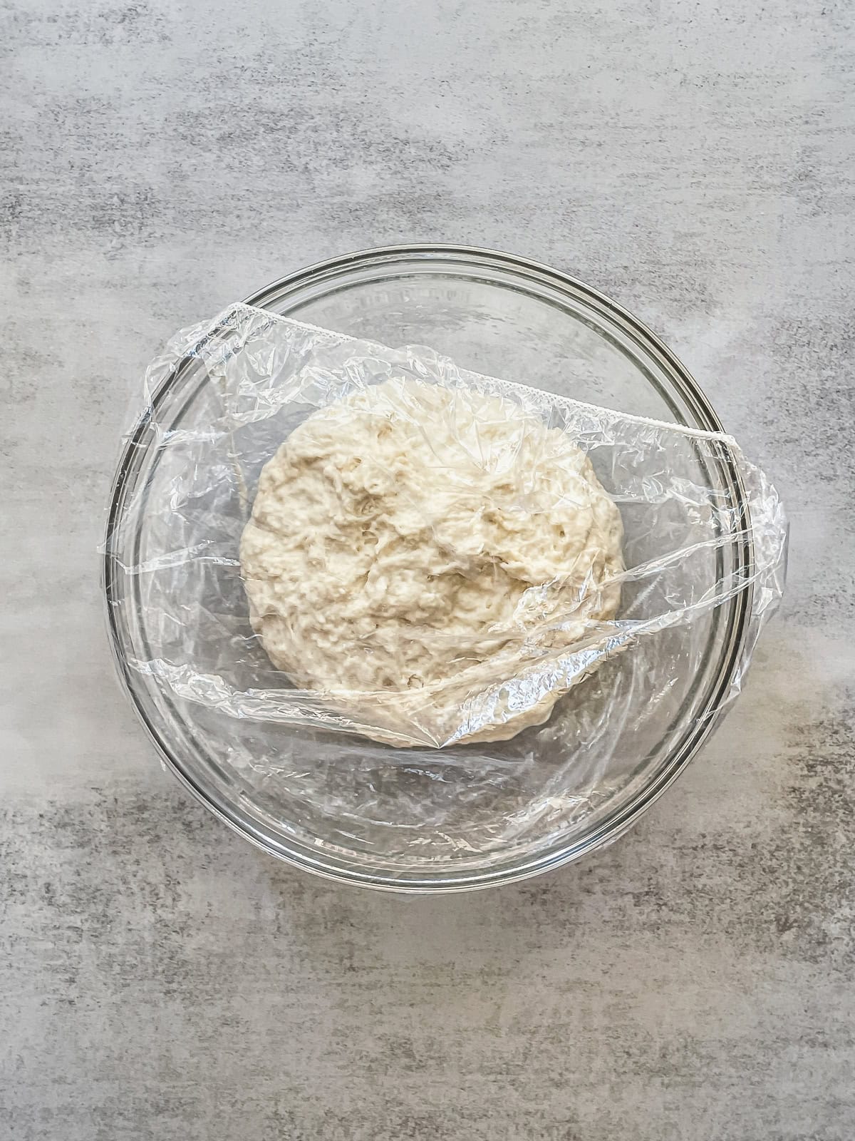 Dough mixture in a mixing bowl, partially covered with a plastic cap.