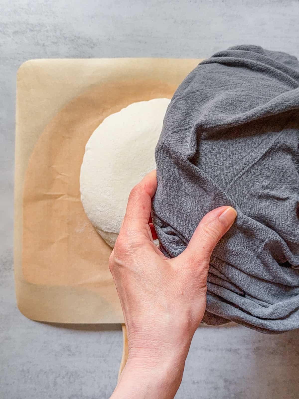 Hands holding a towel-lined bowl with a boule on parchment paper.