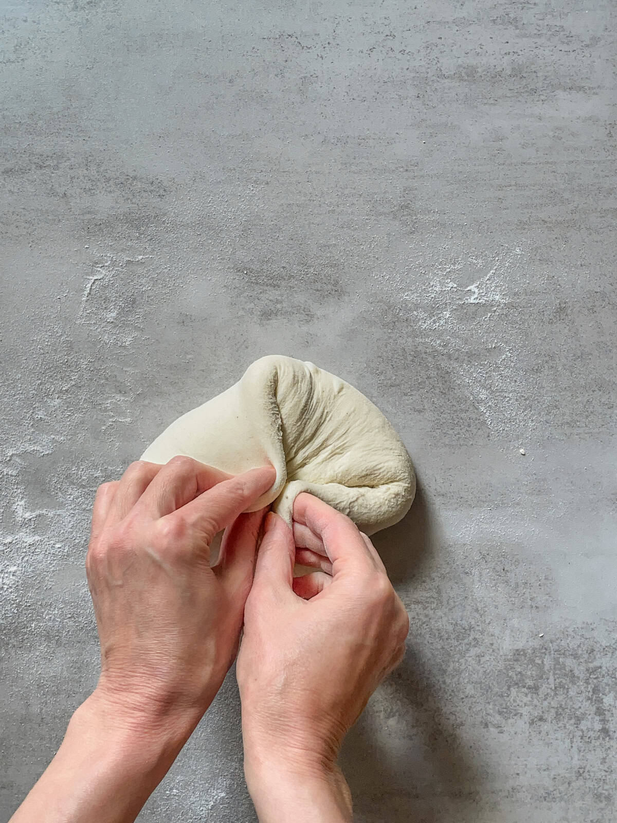 Hands gathering the opposite edges of the dough.
