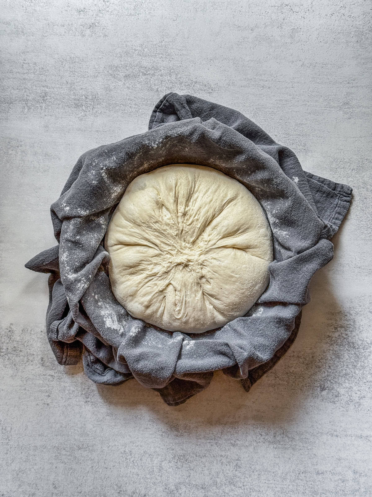 Sourdough boule, seam side up, in a towel-lined bowl.