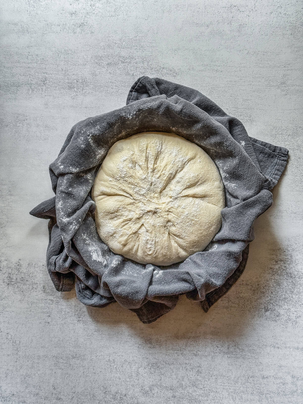 Sourdough boule, dusted with flour, in a towel-lined bowl.