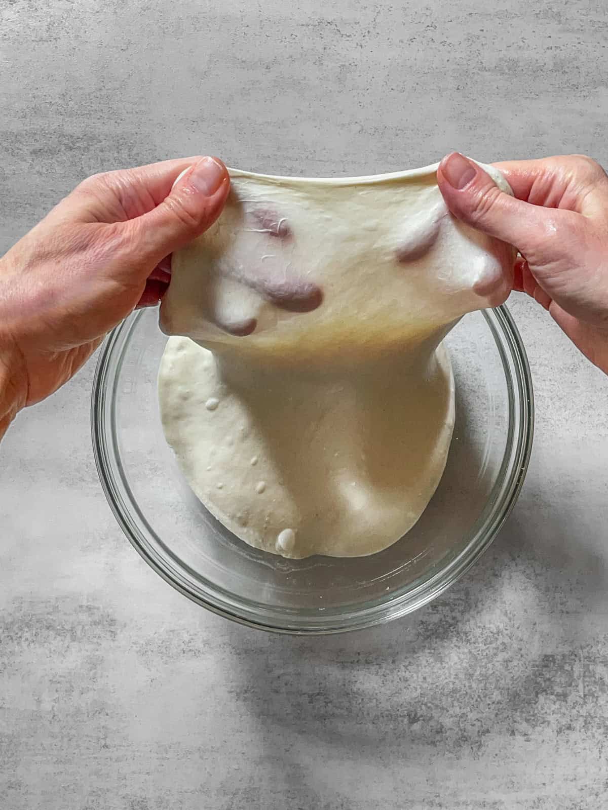 Hands stretching dough in a bowl for the windowpane test.