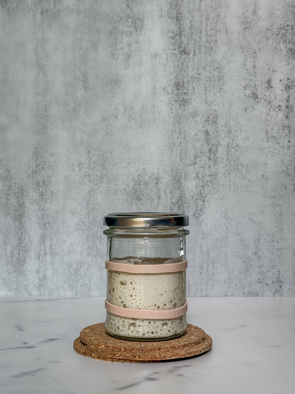 Sourdough starter tripled in a jar, marked with two rubber bands.