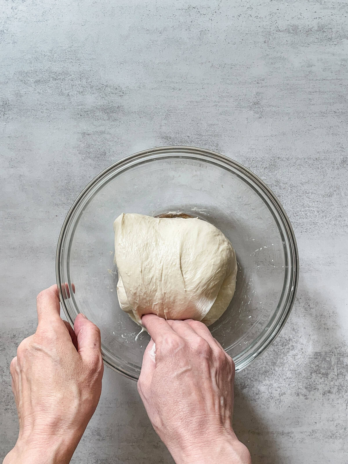 Hand folding bread dough during stretch and folds.