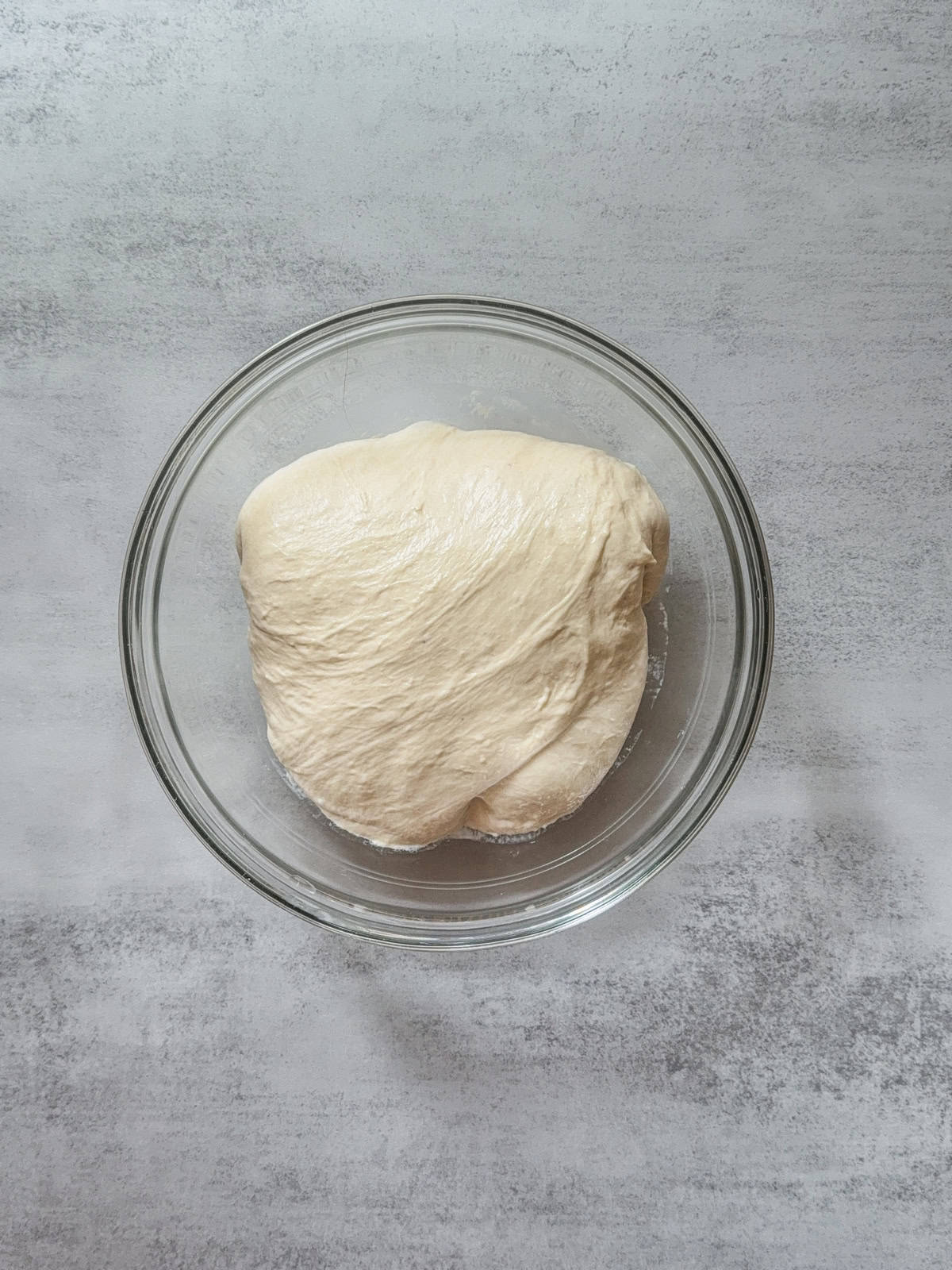 The front edge of bread dough is folded under itself in a glass bowl.