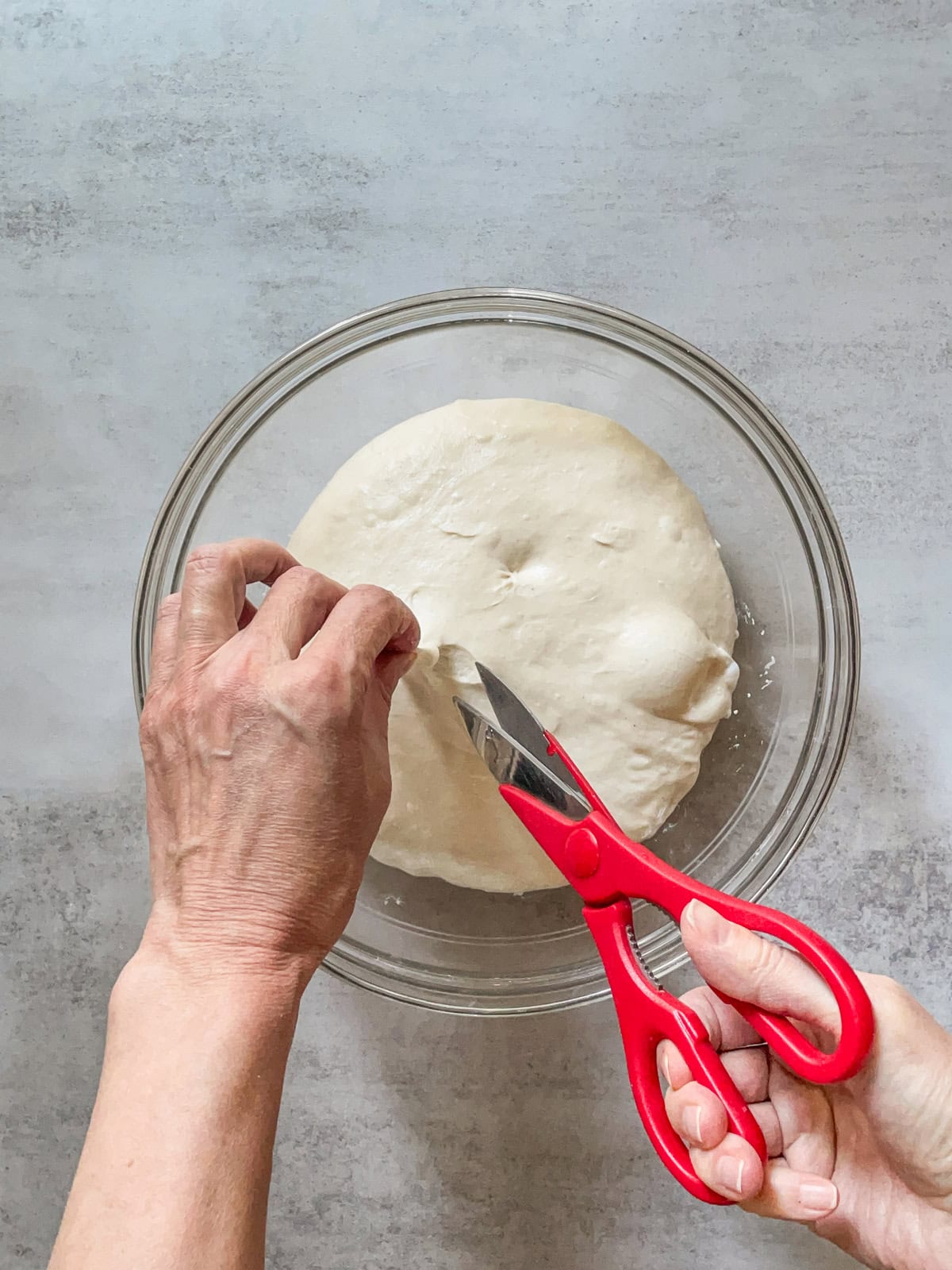 Hands making the second snip in the dough over a glass bowl.
