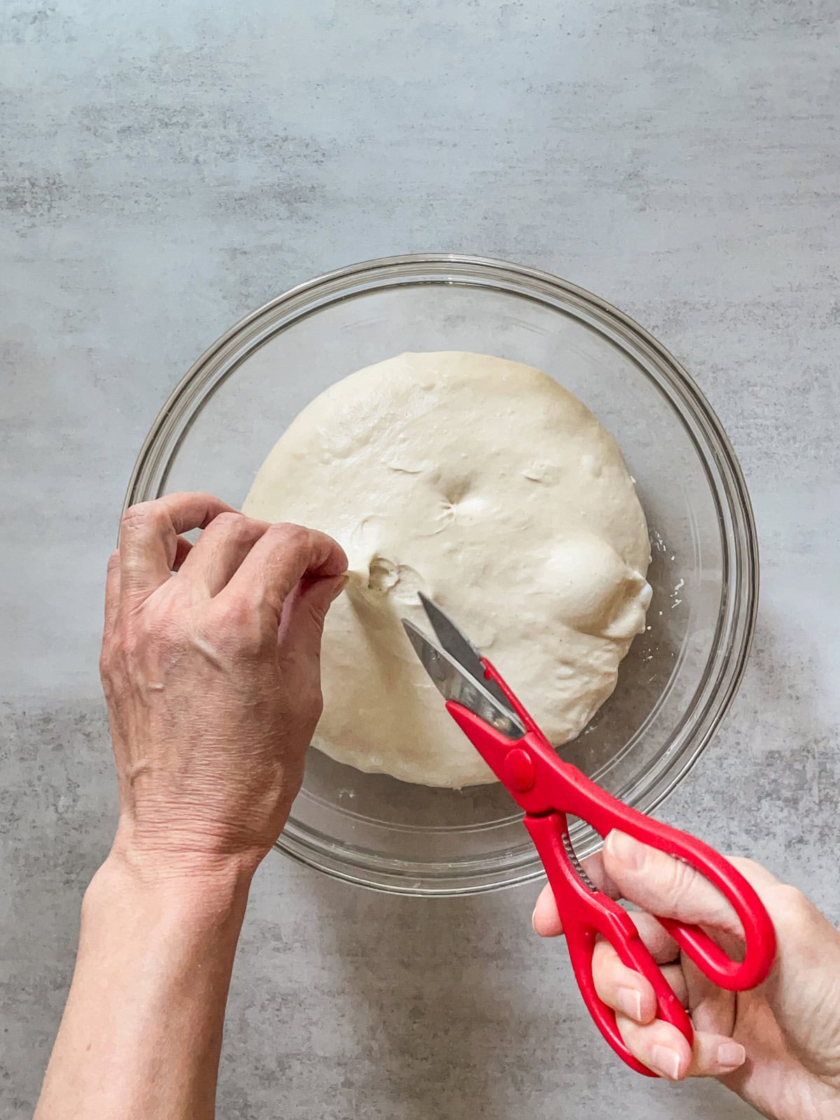 Hands making the third snip in the dough over a glass bowl.