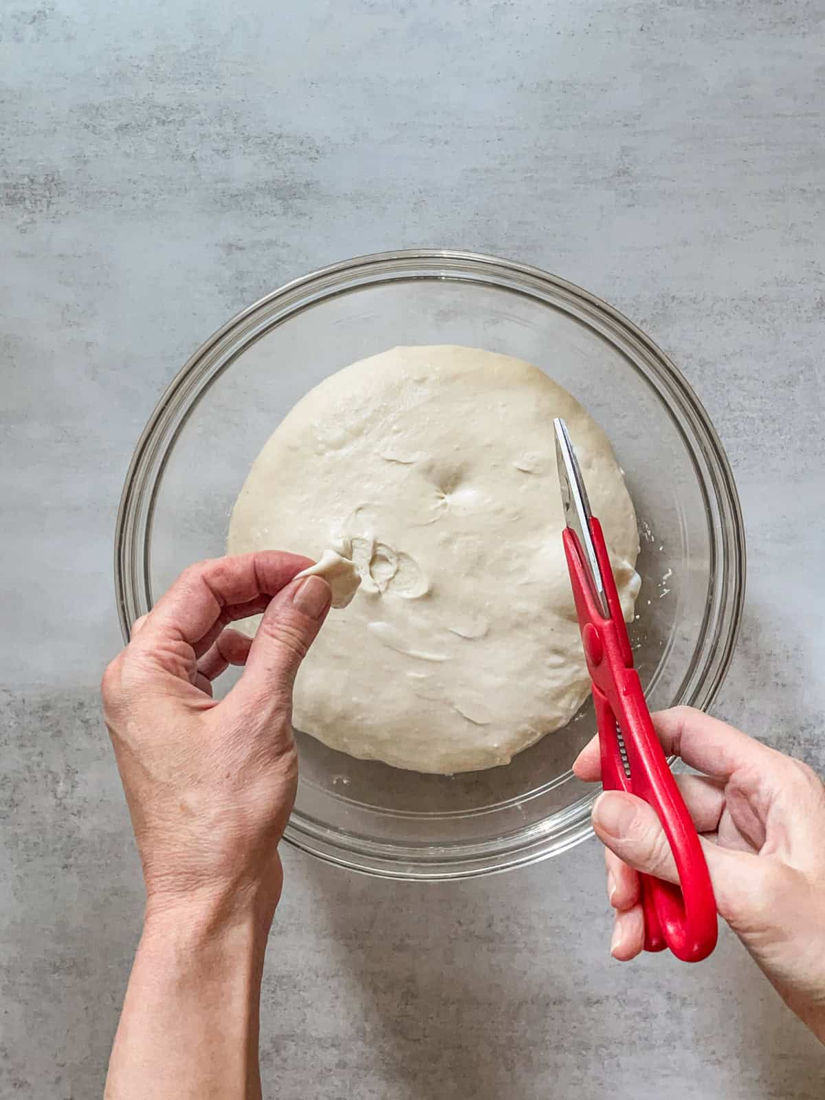 Hands with a piece of dough and scissors over a bowl.