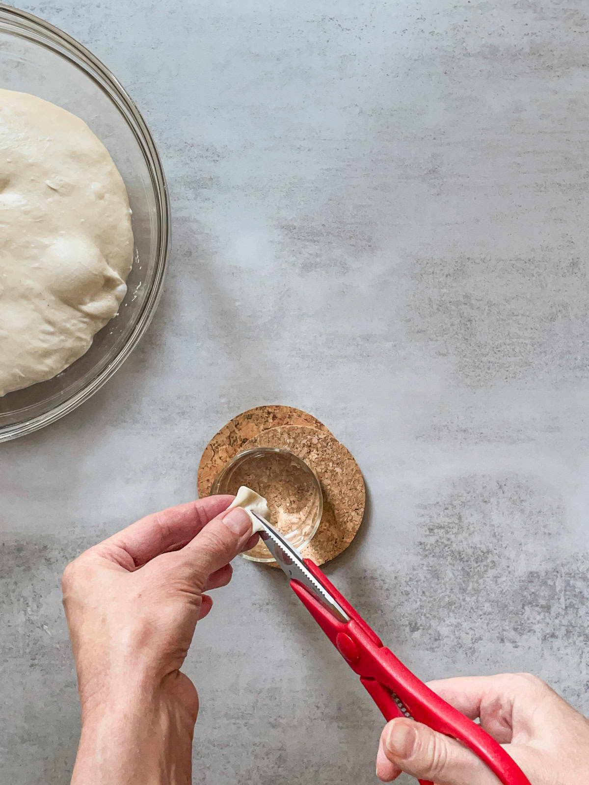 Hands snipping a piece of dough with scissors over a glass with water.