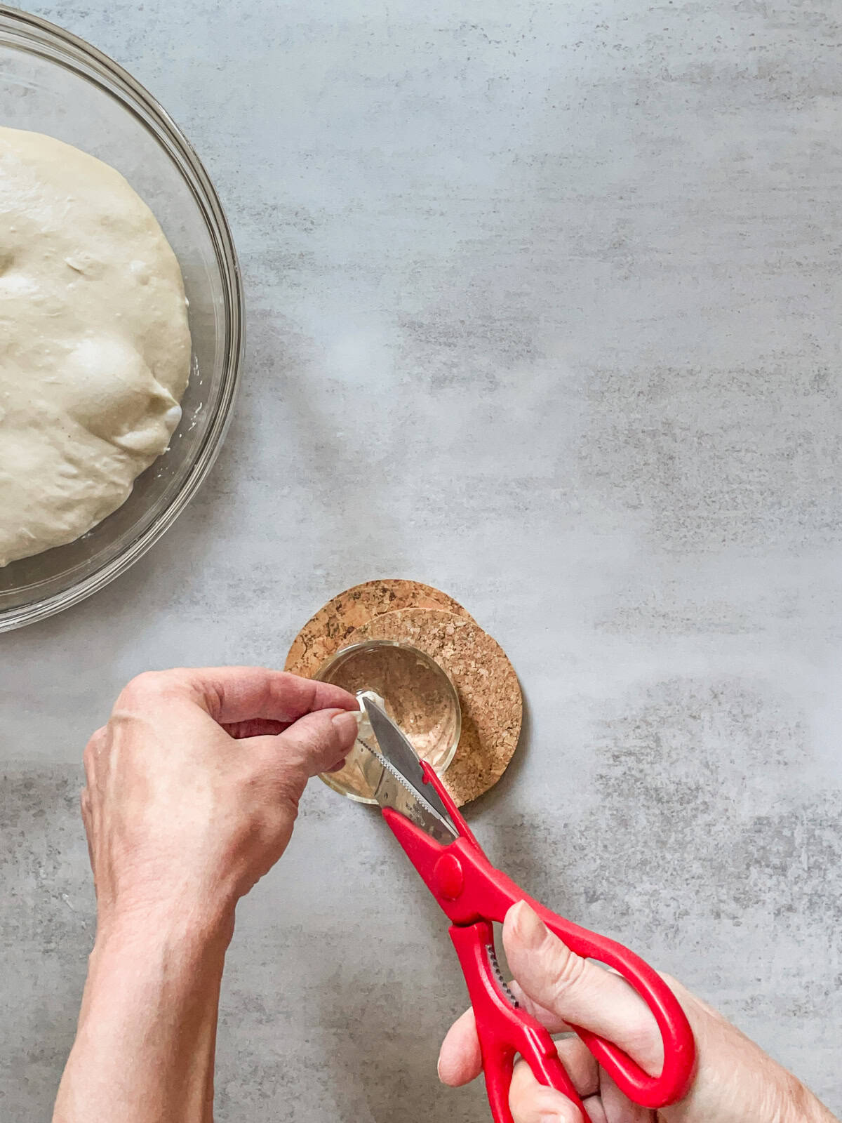 Hands finishing snipping a piece of dough with scissors over a glass of water.