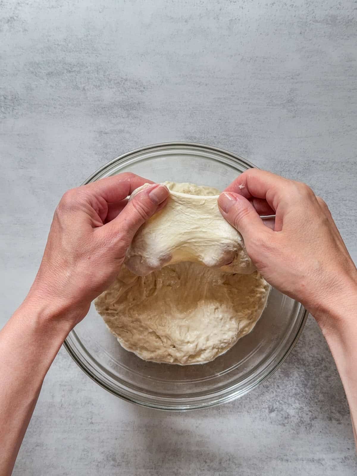 Hands stretching sourdough dough over a glass bowl after fermentolyse.