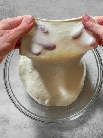 Hands stretching dough during windowpane test.
