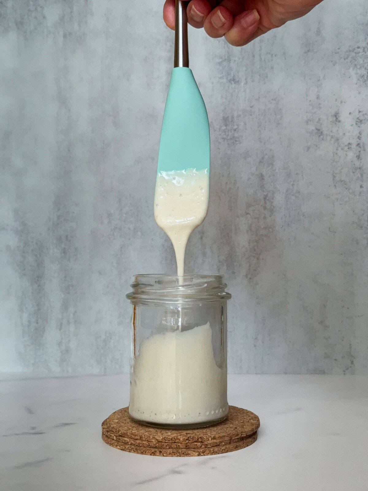 Runny sourdough starter flowing from a spatula into a jar.