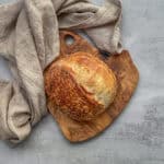 Small batch sourdough bread loaf on a wooden board with a kitchen towel.