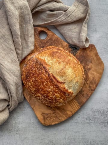 Small batch sourdough bread loaf on a wooden board with a kitchen towel.