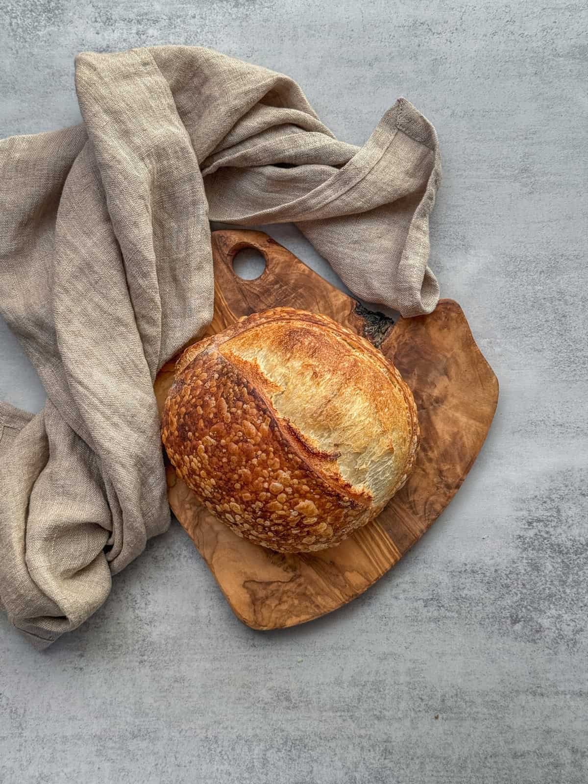 Small batch sourdough bread on a wooden board with a kitchen towel.