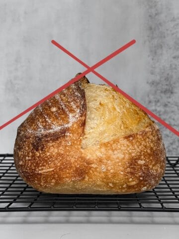Underproofed sourdough bread loaf with a triangle shape on a wooden board.
