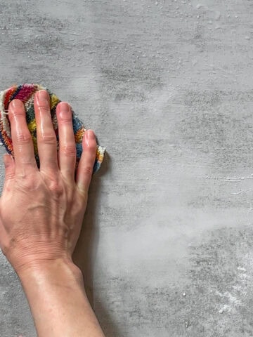 Hand using a dish scrubber to clean a table.