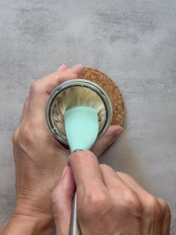 Hands mixing sourdough starter with a jar spatula