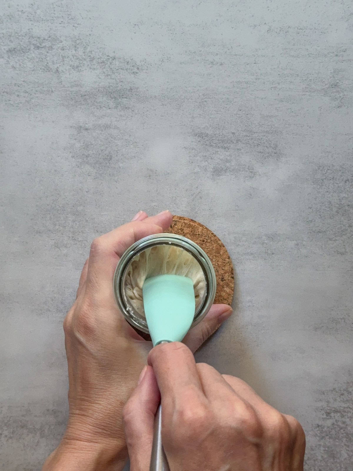 Hands mixing sourdough starter with a spatula.