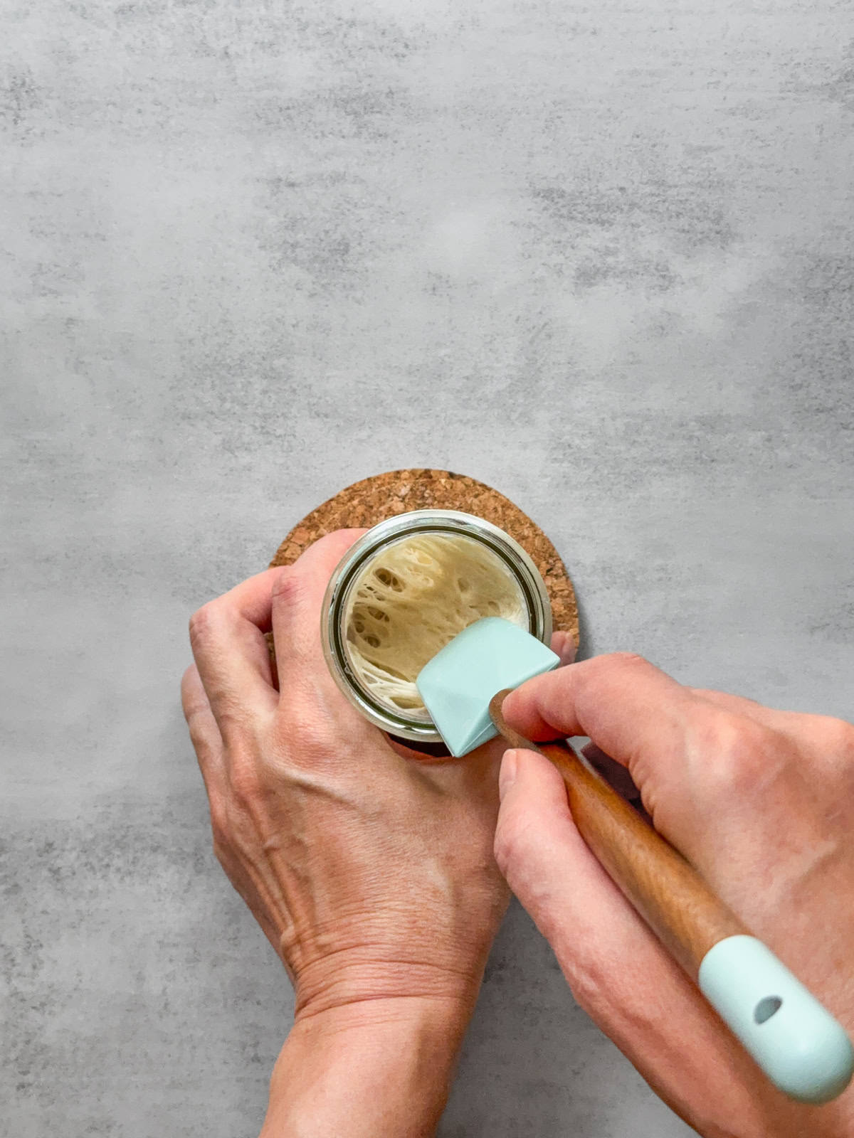 Hands holding a spatula showing 100% hydration sourdough starter texture.