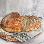 Sliced extra sour sourdough bread in a bread basket lined with a towel.