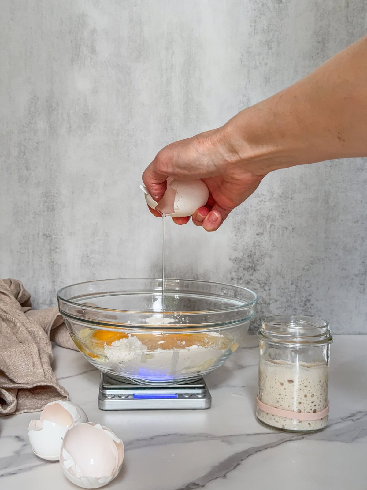 Bowl with flour and sourdough starter, egg being added, illustrating yeast replacement.