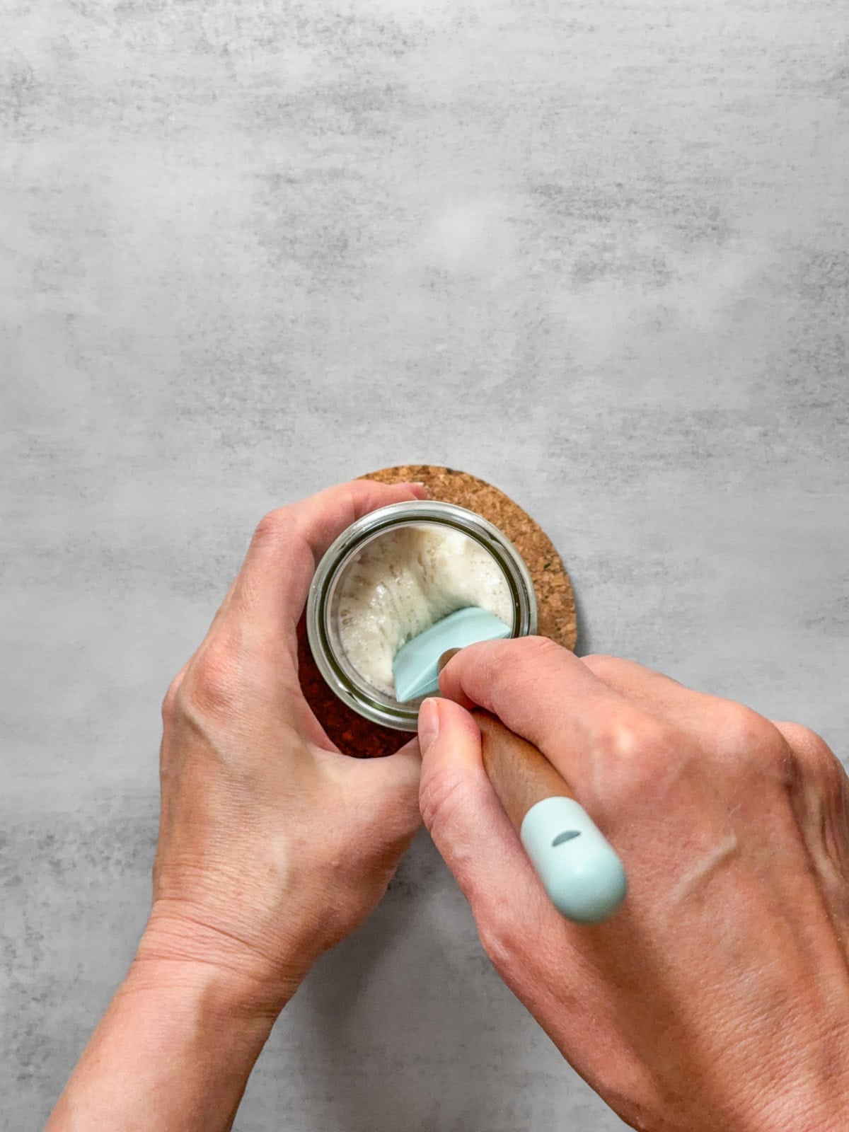 Hands holding a spatula showing liquid sourdough starter texture.