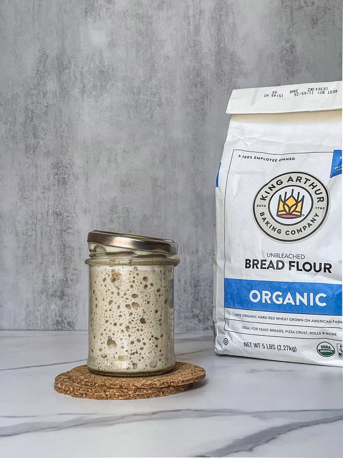 Sourdough starter in a jar next to a bag of flour.