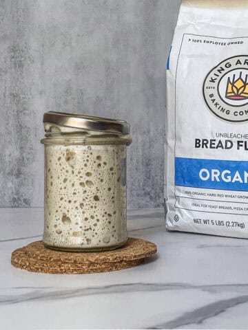 A jar of sourdough starter beside a bag of flour.