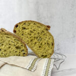 Spinach sourdough bread sliced in half and resting on a kitchen towel.