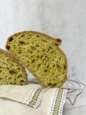 Spinach sourdough bread sliced in half and resting on a kitchen towel.