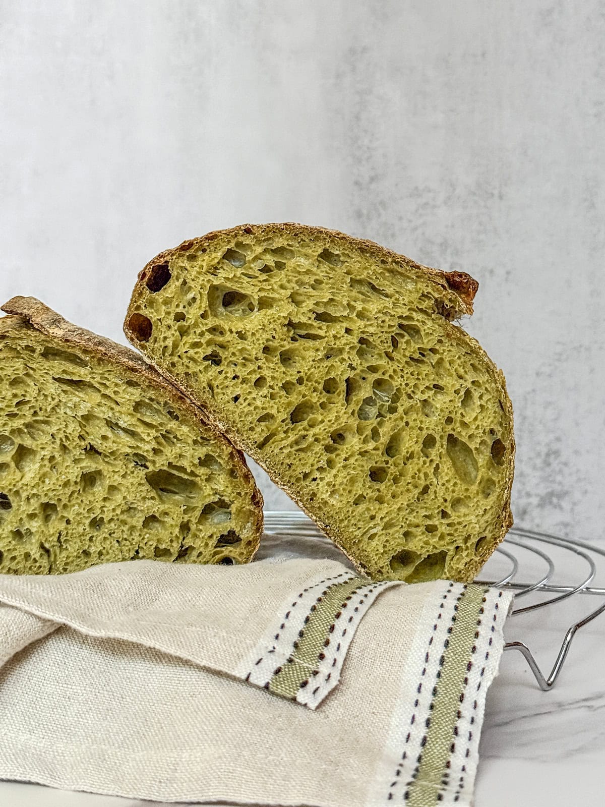 Green spinach sourdough bread sliced in half on a rustic towel.