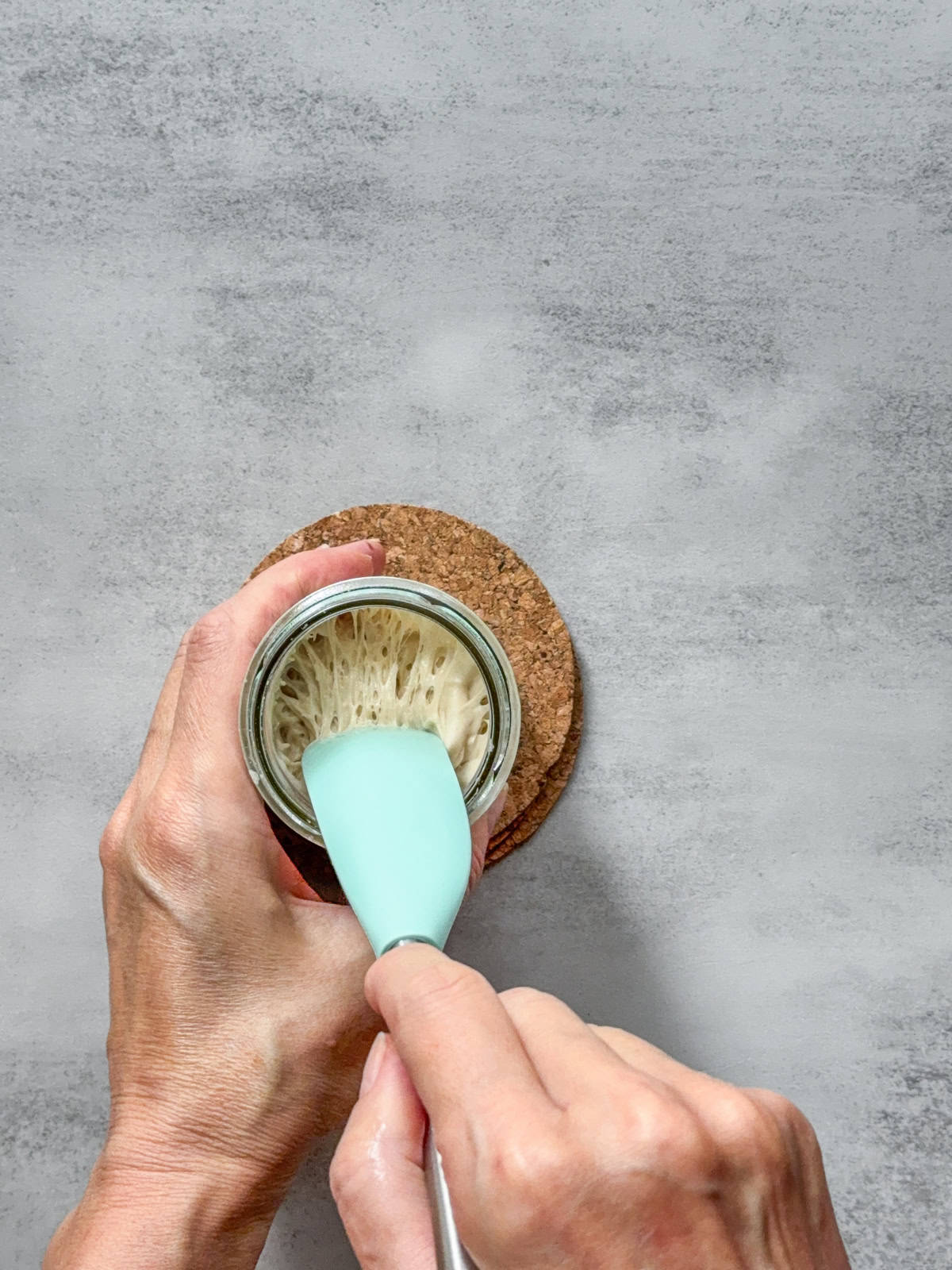 Hands holding a spatula showing stiff sourdough starter texture.