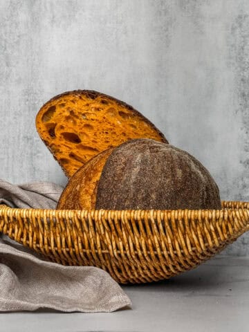 Carrot sourdough bread loaf sliced in half in a bread basket.