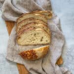 No-knead sourdough bread slices on a wooden board with a linen cloth.