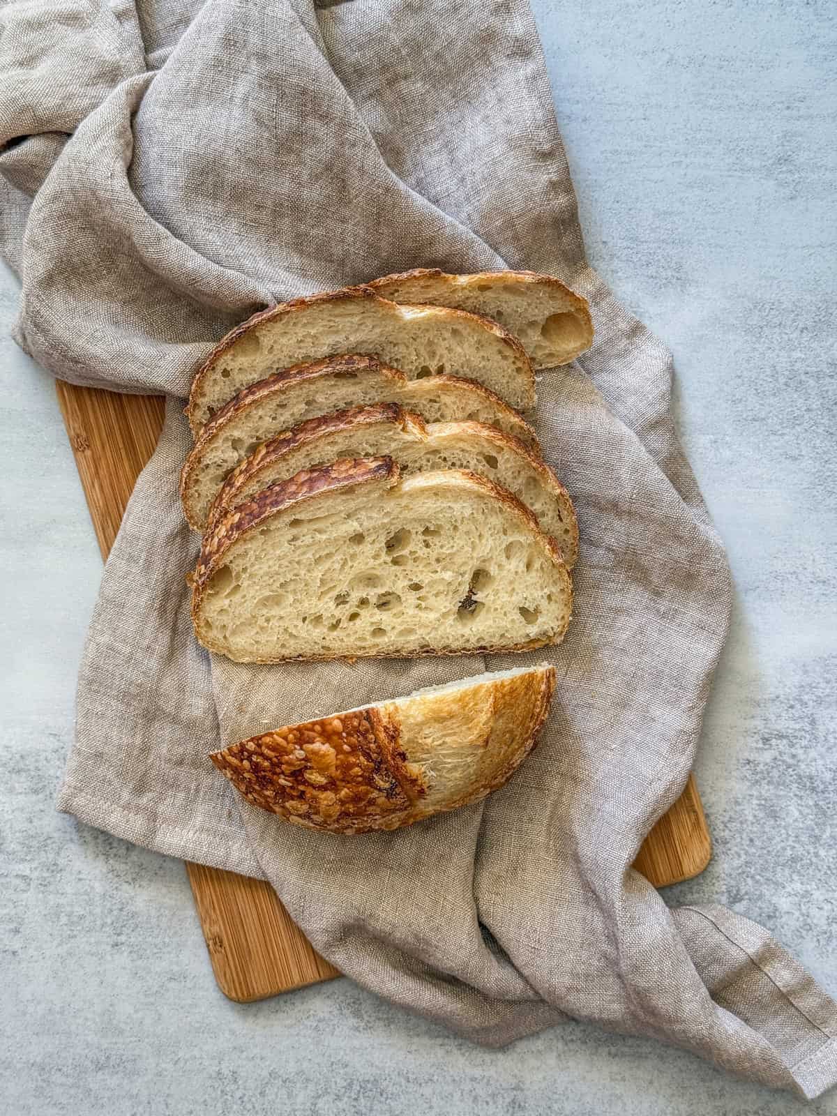 Fresh no-knead sourdough bread slices on a wooden board with a linen cloth.