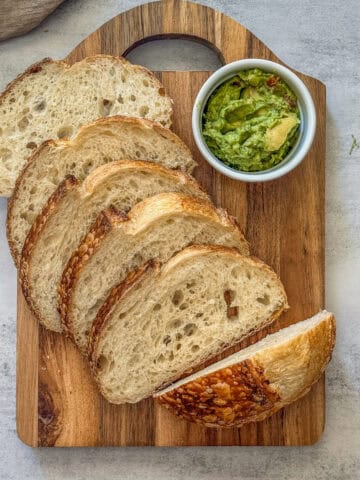 Fresh overnight sourdough bread sliced on a cutting board with guacamole.