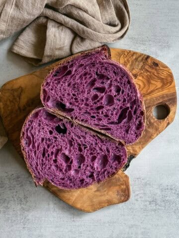 Purple sweet potato sourdough bread loaf sliced in half on a wooden board.
